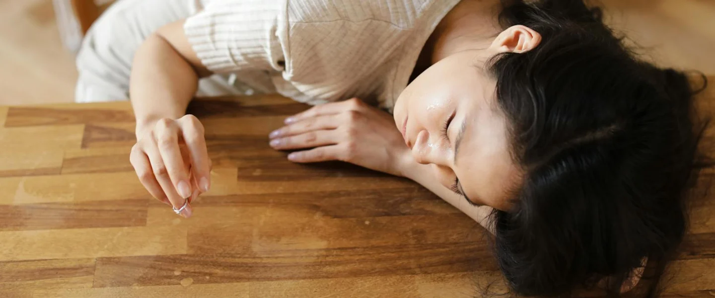 A woman lying sadly at a wooden table, holding a wedding ring, conveying emotions of separation and loss.
